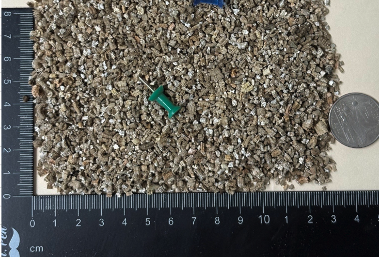 Fine grade expanded vermiculite particles shown next to a ruler and coin for scale reference