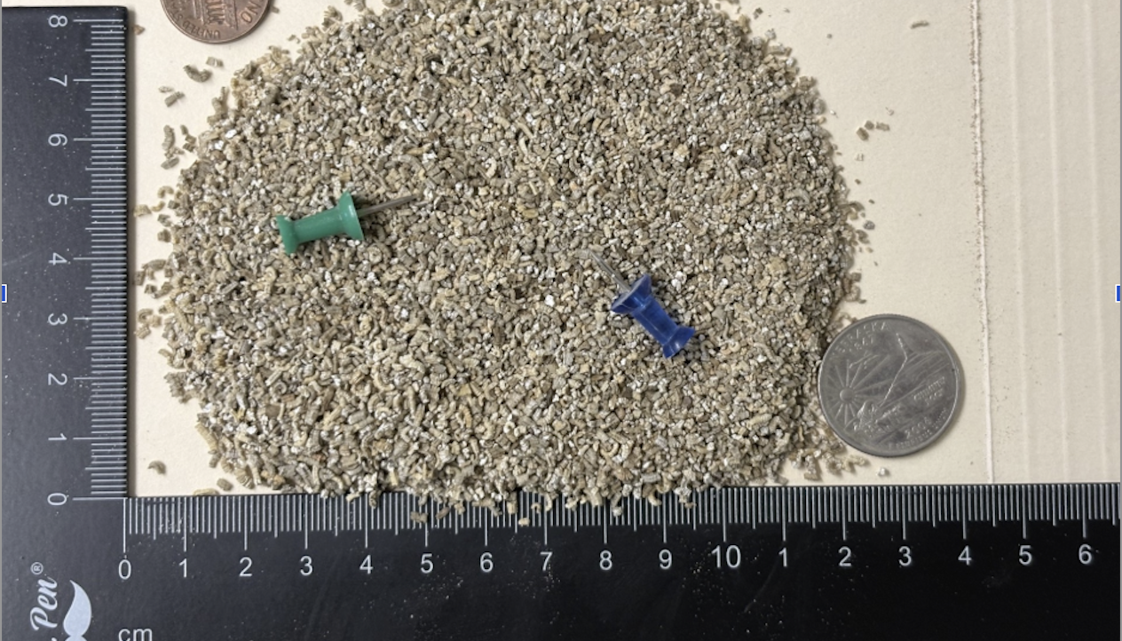 Super fine grade expanded vermiculite particles shown next to a ruler and coin for scale reference