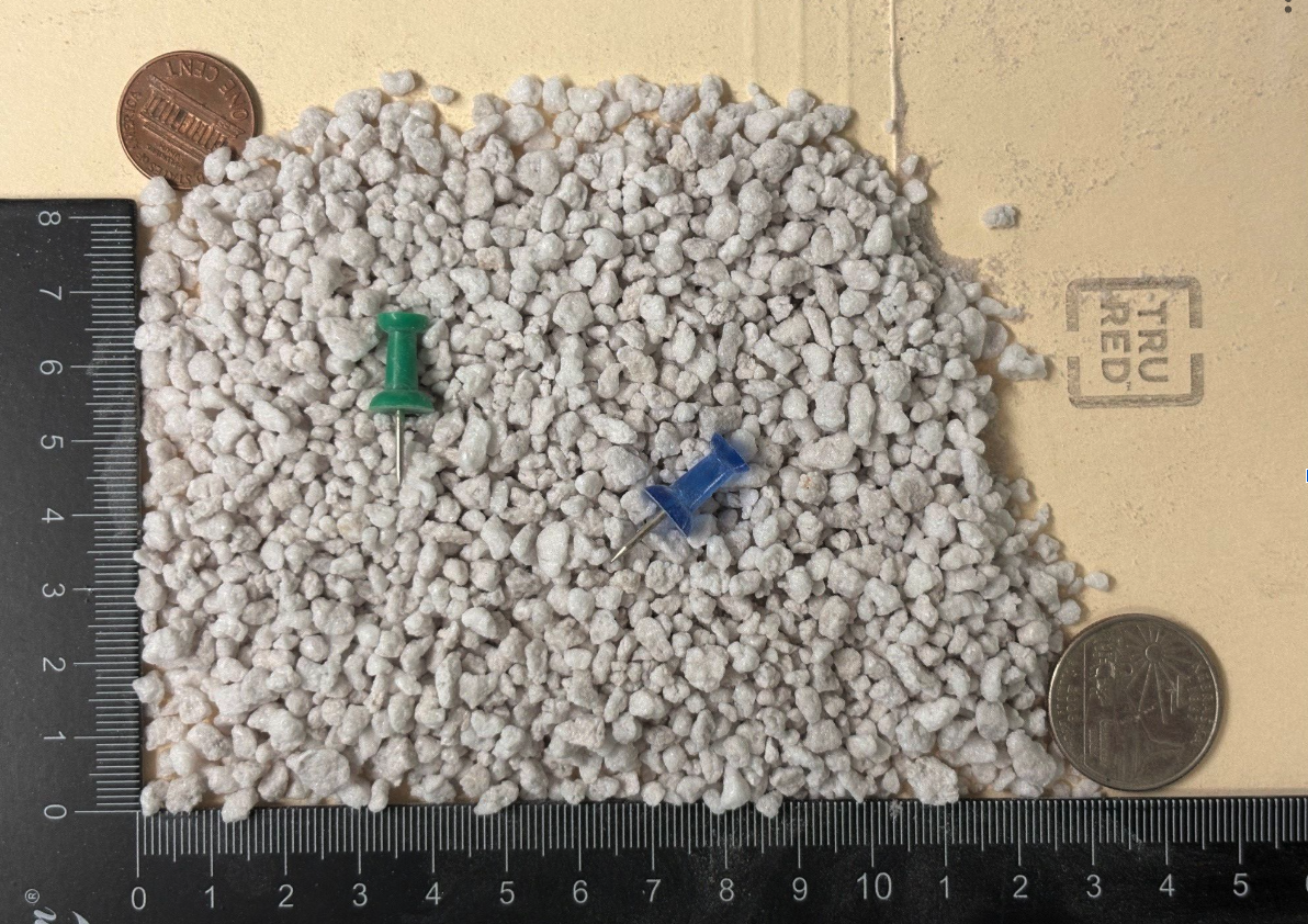 Coarse grade expanded perlite particles shown next to a ruler and coin for scale reference