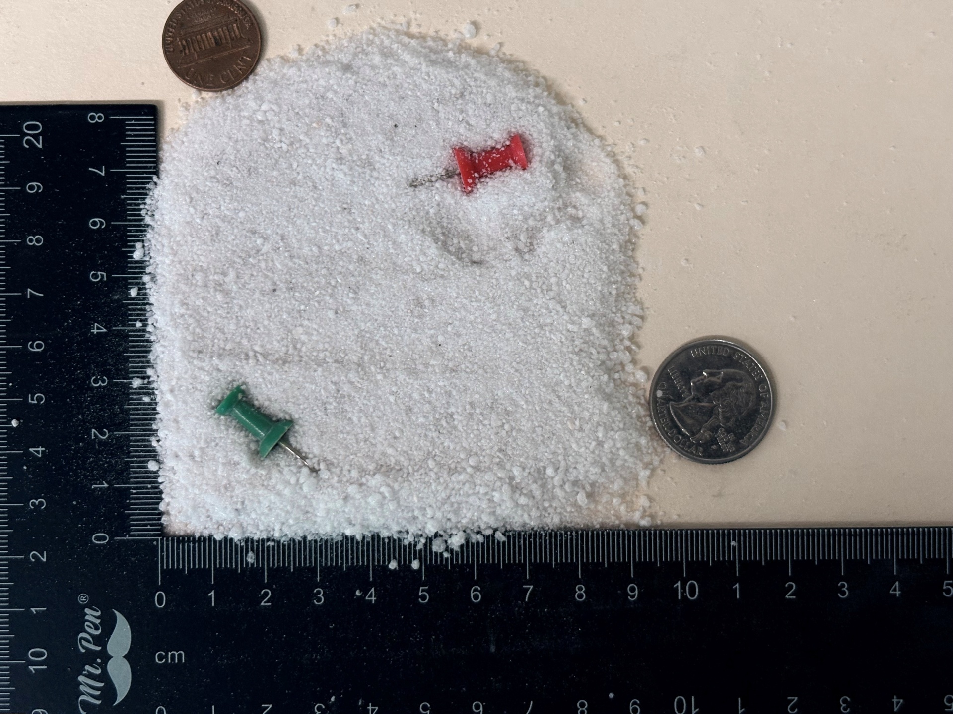 Cryogenic grade expanded perlite particles shown next to a ruler, coins, and push pins for scale reference