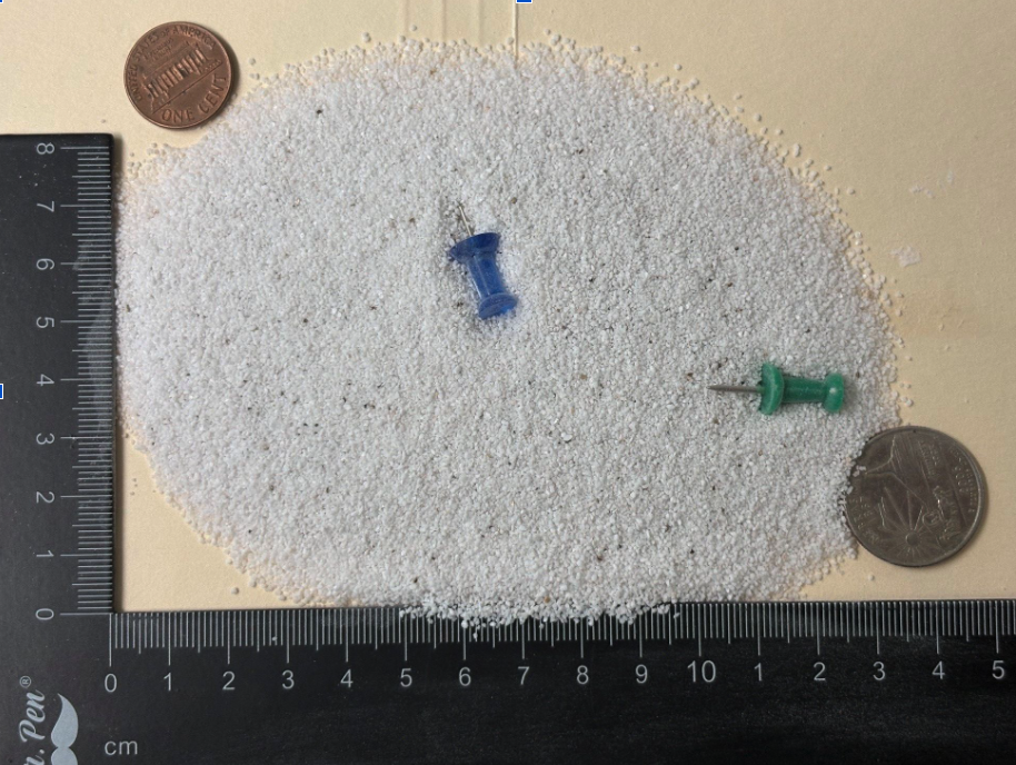 Fine grade expanded perlite particles shown next to a ruler and coin for scale reference