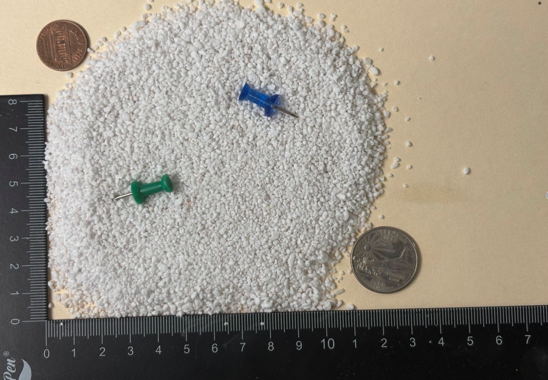 Medium grade expanded perlite particles shown next to a ruler and coin for scale reference