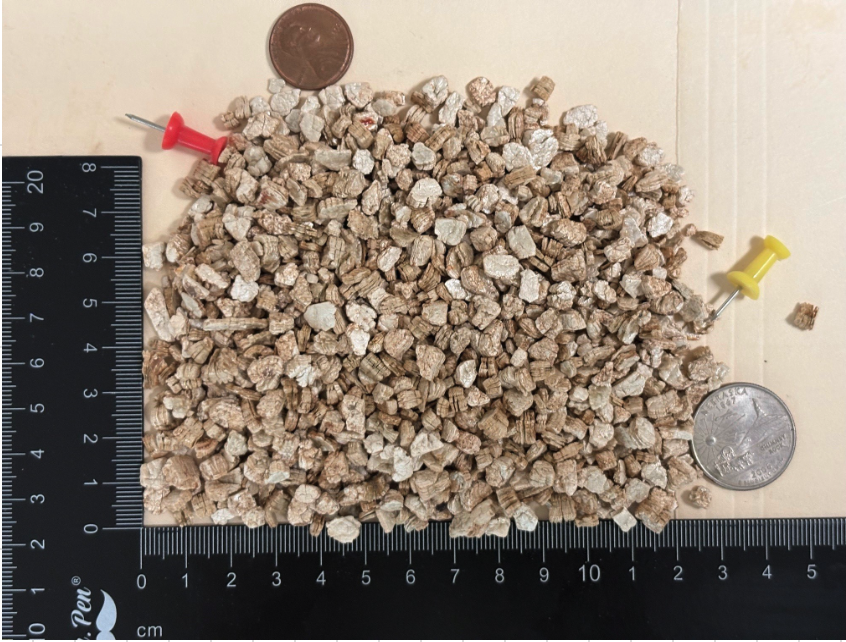 Medium grade expanded vermiculite particles shown next to a ruler and coin for scale reference