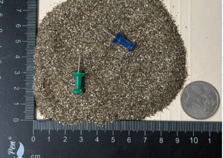 Micron ultra-fine grade expanded vermiculite particles shown next to a ruler and coin for scale reference